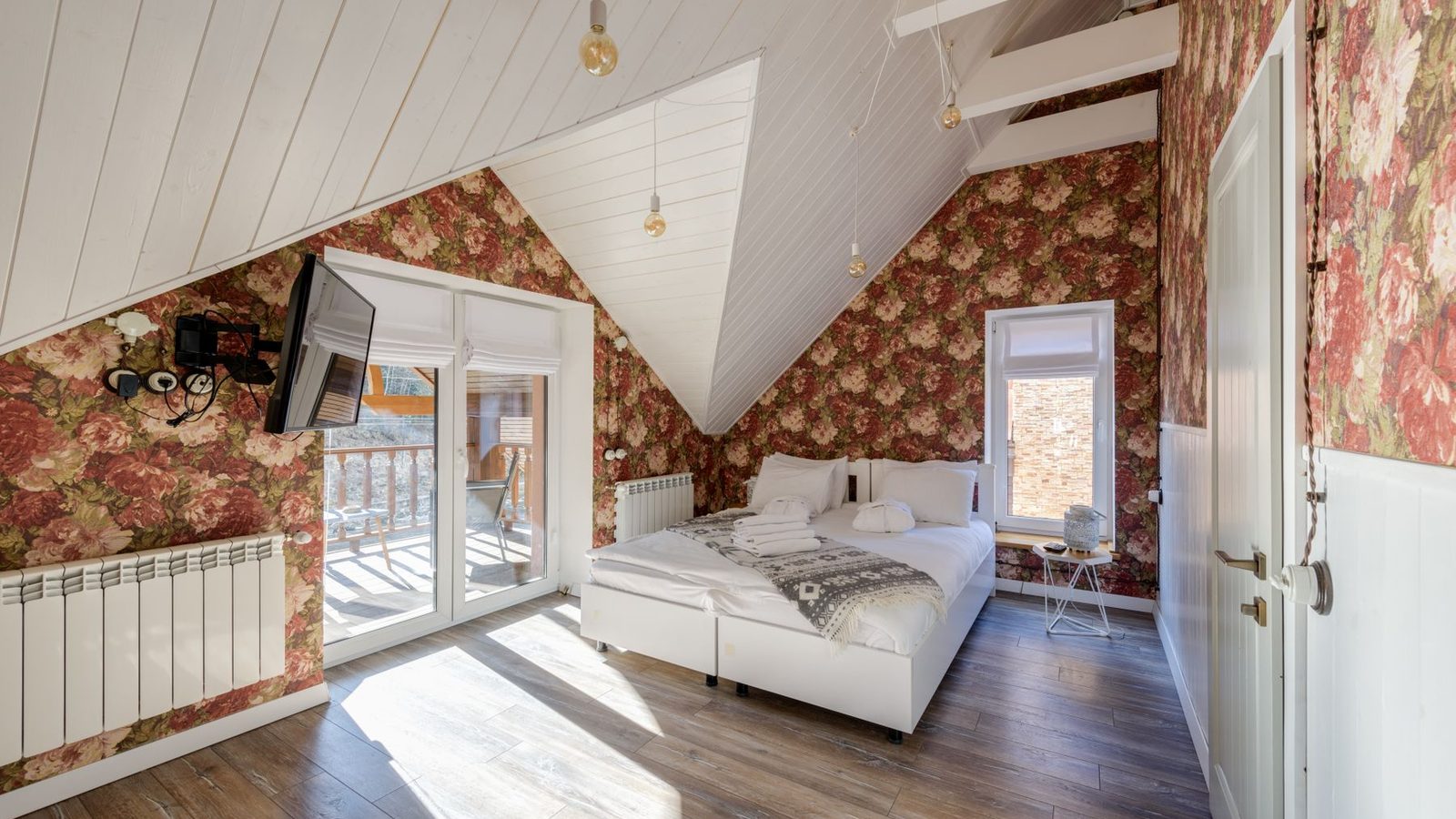 A sunlit attic bedroom with red floral wallpaper on the walls